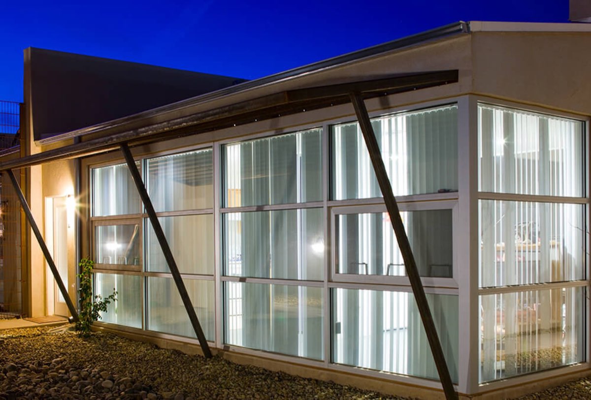 Glass-walled community building at Lo Lomas glowing from within at dusk